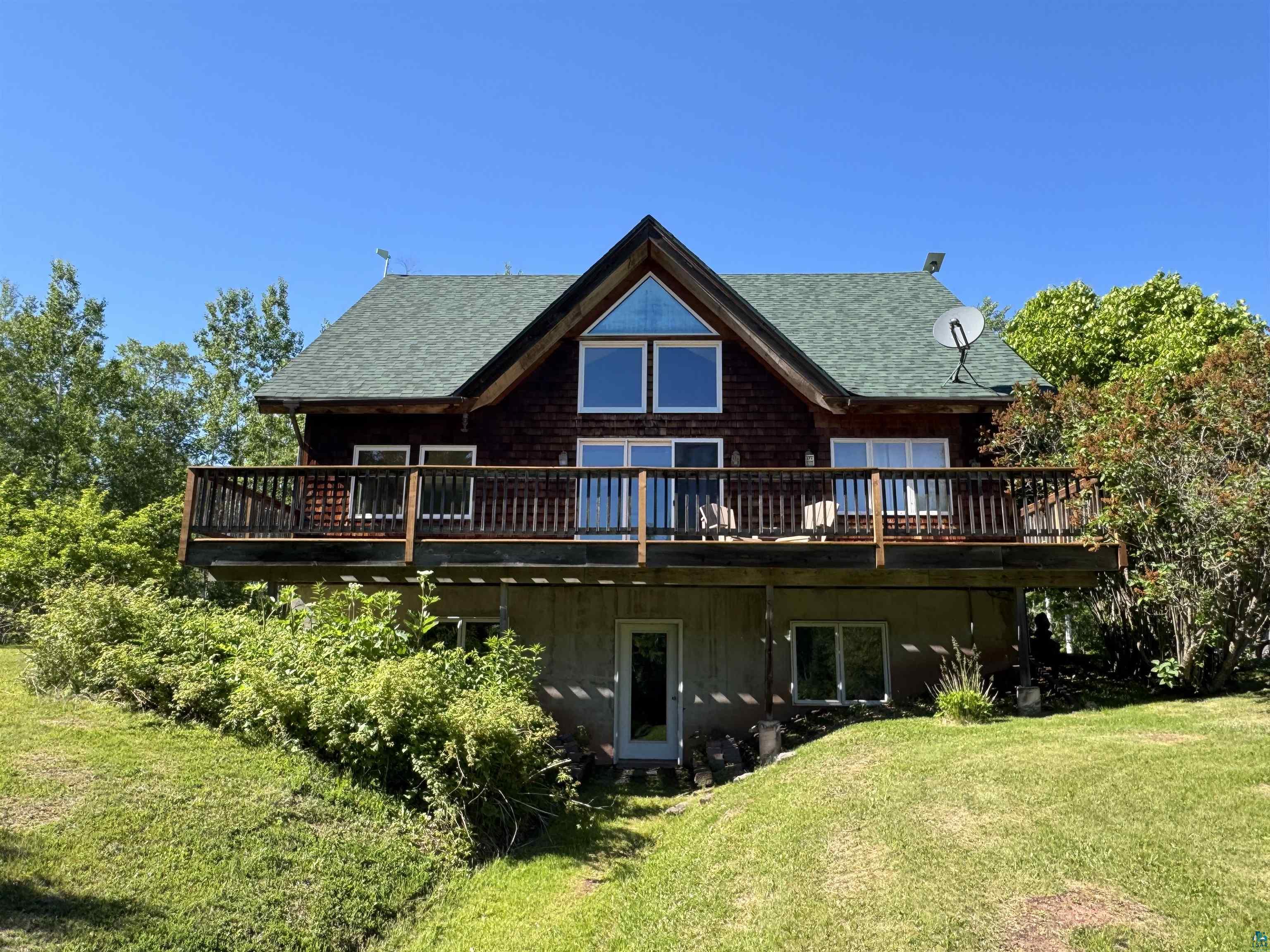 1745 Becks Road Maple, WI 54854 - Photo 1 of 50 Two-story property featuring a prominent deck with wooden railings, a green shingled roof, and a visible walk-out lower level