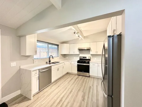 a large kitchen with a stove a sink dishwasher a refrigerator and white cabinets with wooden floor