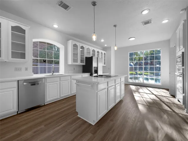 a large kitchen with kitchen island granite countertop a stove a sink a refrigerator and white cabinets with wooden floor