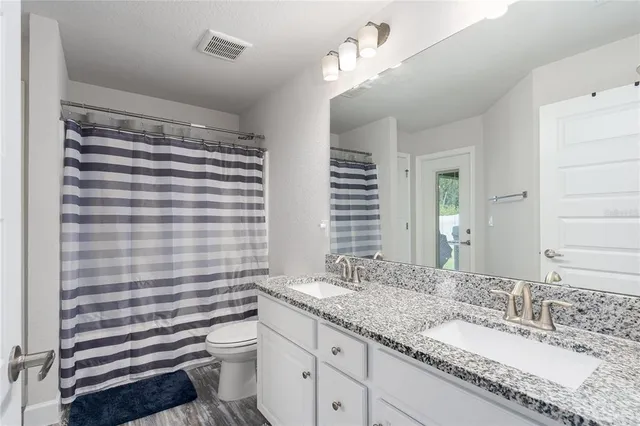 a bathroom with a granite countertop sink a toilet a mirror and shower curtain