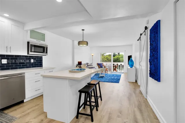 a kitchen with stainless steel appliances kitchen island granite countertop a refrigerator a stove a sink dishwasher and white cabinets with wooden floor