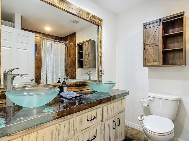 a bathroom with a granite countertop sink a toilet a mirror and shower