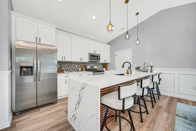 a kitchen with stainless steel appliances granite countertop a refrigerator a sink dishwasher a stove and white cabinets with wooden floor