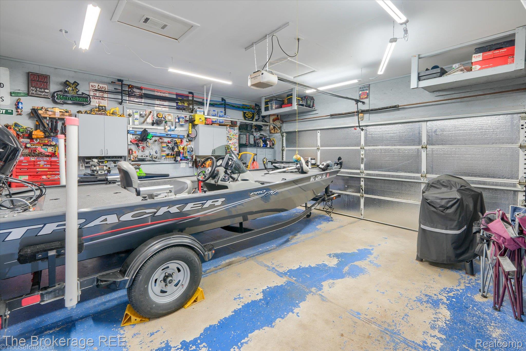 4432 North Belsay Road Flint, MI 48506 - Photo 49 of 79 Attached garage space featuring overhead fluorescent lighting, built-in wall cabinetry, pegboard tool organization, and a roll-up insulated garage door