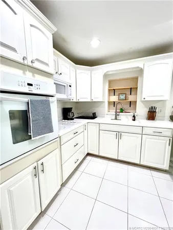 a kitchen with granite countertop white cabinets white appliances a sink and a window