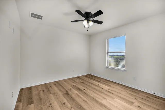 a view of empty room with wooden floor and ceiling fan