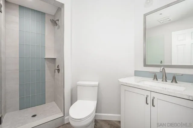 a bathroom with a granite countertop toilet a sink a mirror and shower