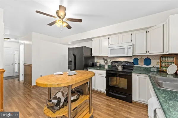 a kitchen with stainless steel appliances kitchen island granite countertop a sink a stove a refrigerator a microwave oven with white cabinets and wooden floor