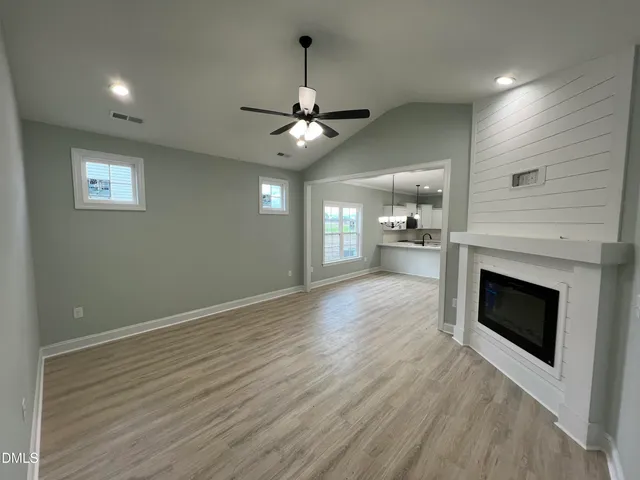 an empty room with wooden floor a ceiling fan a fireplace and windows