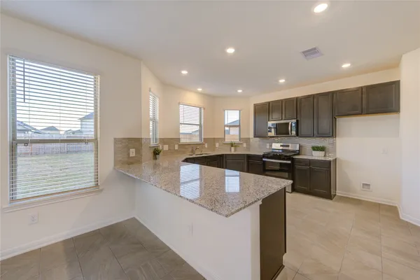 a kitchen with kitchen island granite countertop a stove top oven a sink a refrigerator and white cabinets