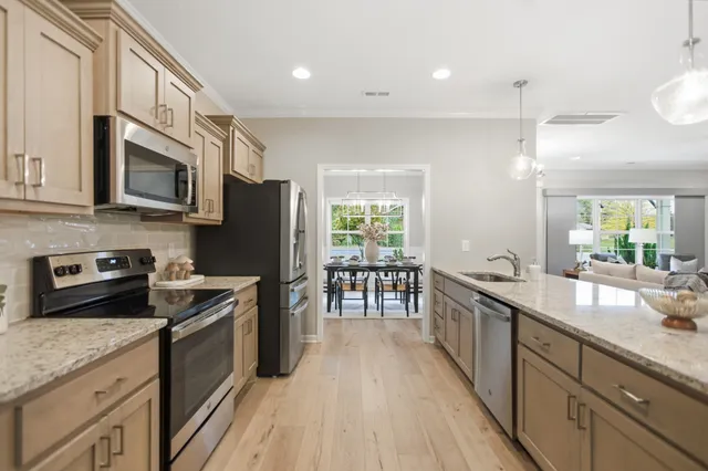 a kitchen with stainless steel appliances granite countertop a stove top oven a sink dishwasher a refrigerator and a dining table with wooden floor