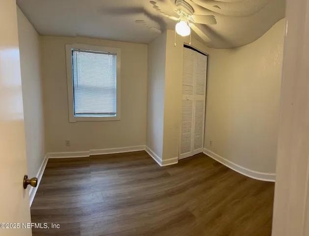 an empty room with wooden floor fan and windows