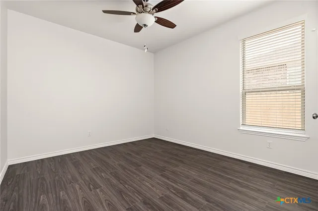 an empty room with wooden floor fan and windows