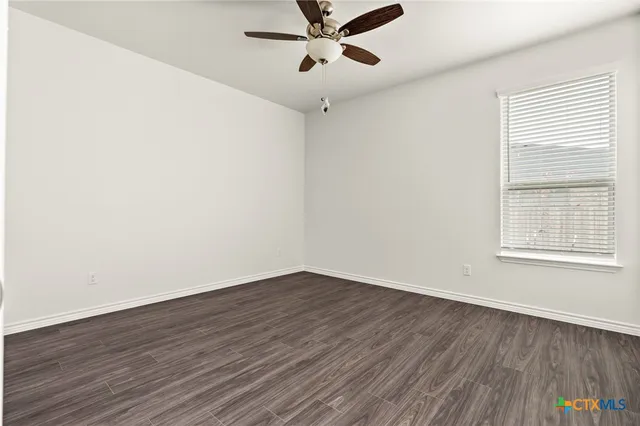 an empty room with wooden floor fan and windows