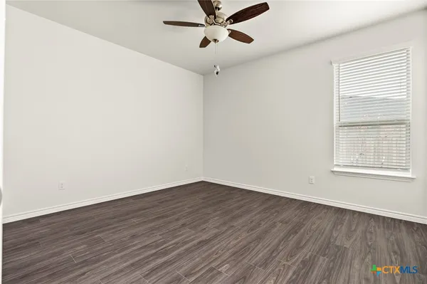 an empty room with wooden floor fan and windows