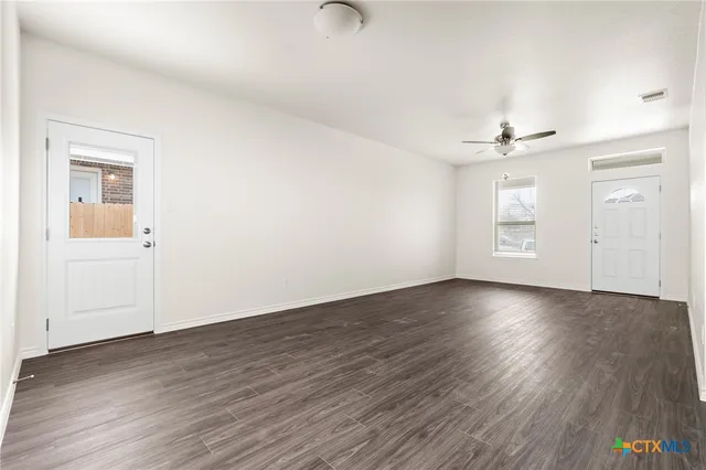 an empty room with wooden floor chandelier and windows
