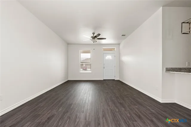 an empty room with wooden floor chandelier fan and windows