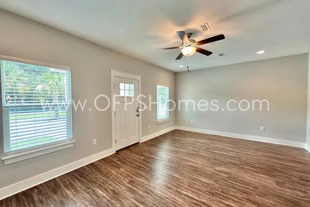 an empty room with wooden floor fan and windows