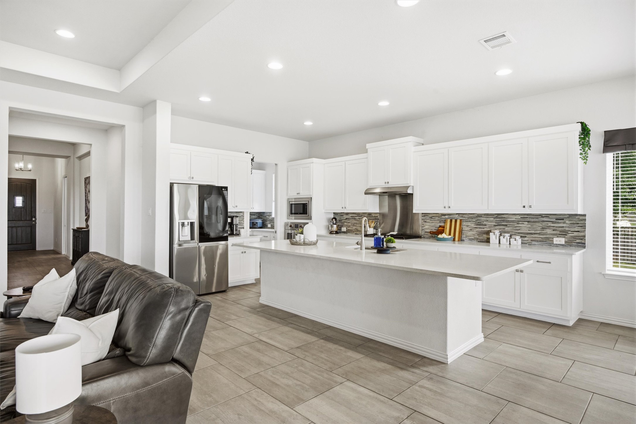192 Raptor Beak Way Cedar Creek, TX 78612 - Photo 7 of 38 Modern kitchen featuring white cabinetry, stainless steel appliances, a white island, and a textured tile backsplash