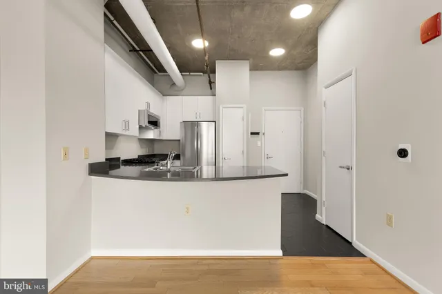 a kitchen with stainless steel appliances granite countertop a refrigerator a sink dishwasher a stove and white countertops with wooden floor