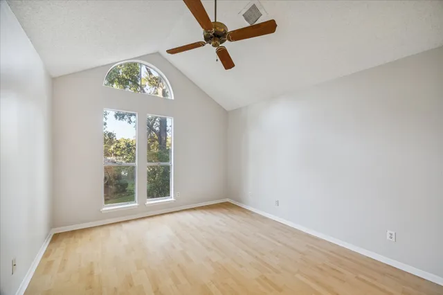 an empty room with wooden floor fan and windows