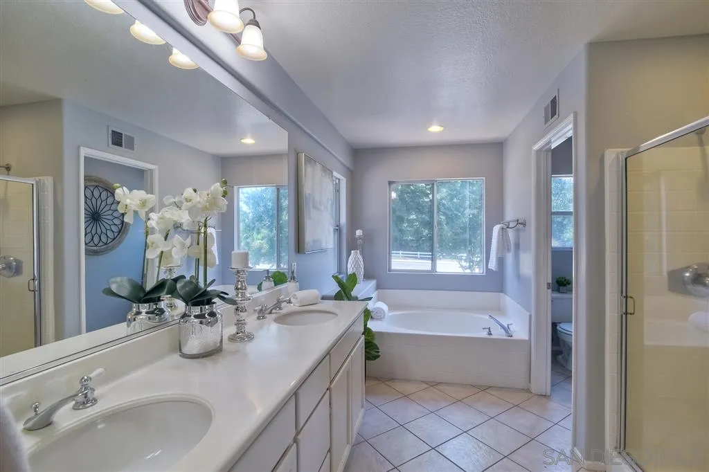 11574 Village Ridge Road San Diego, CA 92131 - Photo 17 of 25 a bathroom with a double vanity sink a large mirror a bathtub and next to a window
