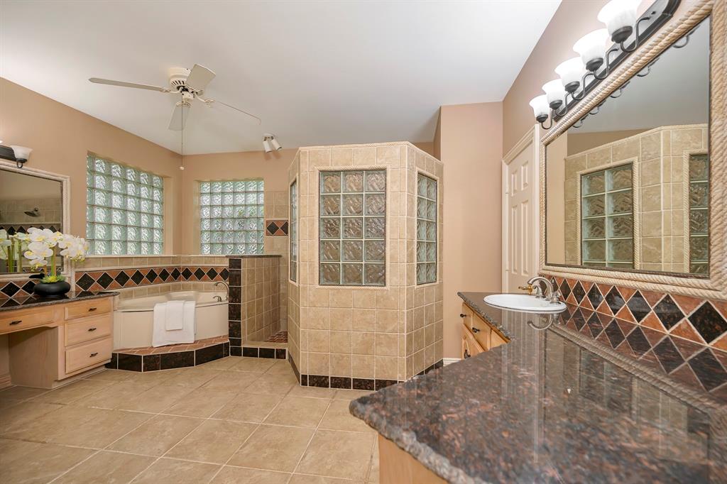 4008 Ramsgate Court Colleyville, TX 76034 - Photo 6 of 33 Spacious bathroom featuring a corner soaking tub, a tiled walk-in shower with glass block windows, and dual vanities with dark stone countertops