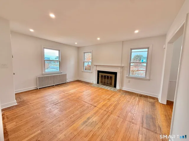 an empty room with wooden floor fireplace and windows
