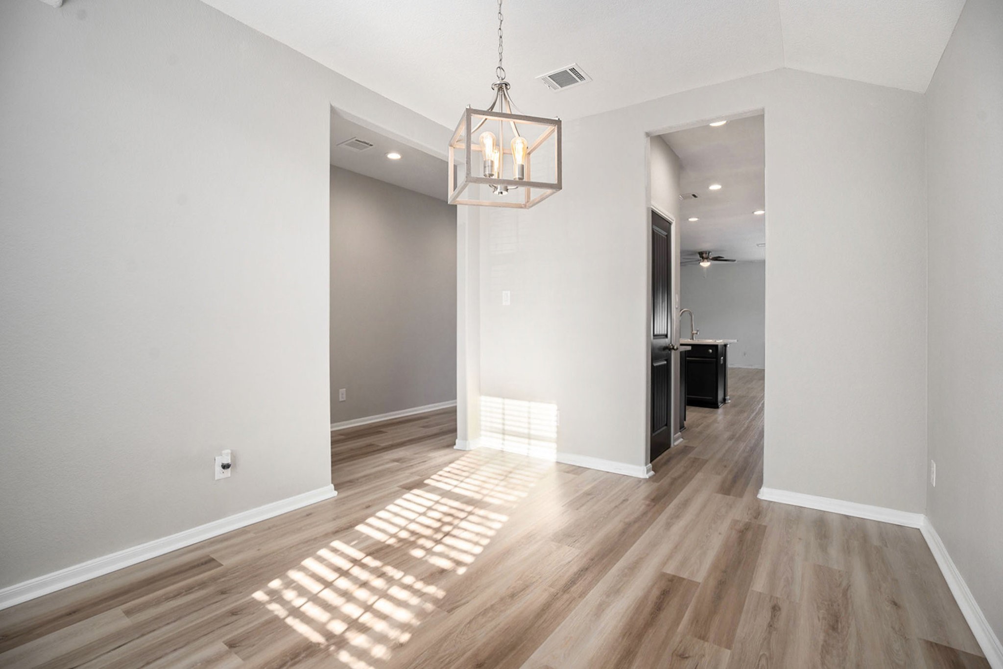 4027 Spurwing Lane Baytown, TX 77521 - Photo 14 of 34 This photo showcases a bright dining area just inside the entryway to the right. A contemporary light fixture hangs from the ceiling, and the space leads to an open kitchen area. The pantry door is seen through the opening.