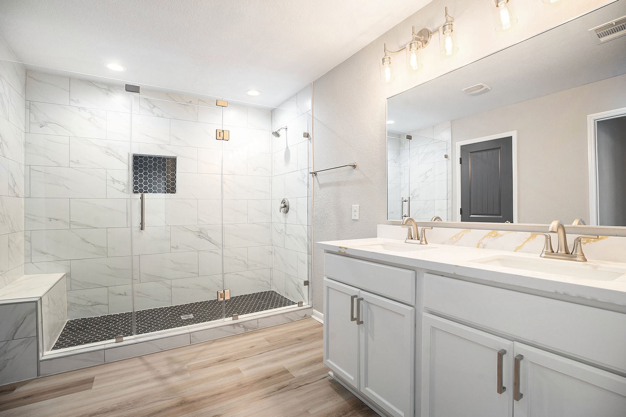 4027 Spurwing Lane Baytown, TX 77521 - Photo 23 of 34 The primary bathroom features a spacious glass-enclosed shower with elegant tiles and a built-in bench. It includes a double vanity with a large mirror, modern light fixtures, and sleek fixtures, creating a luxurious and functional space.