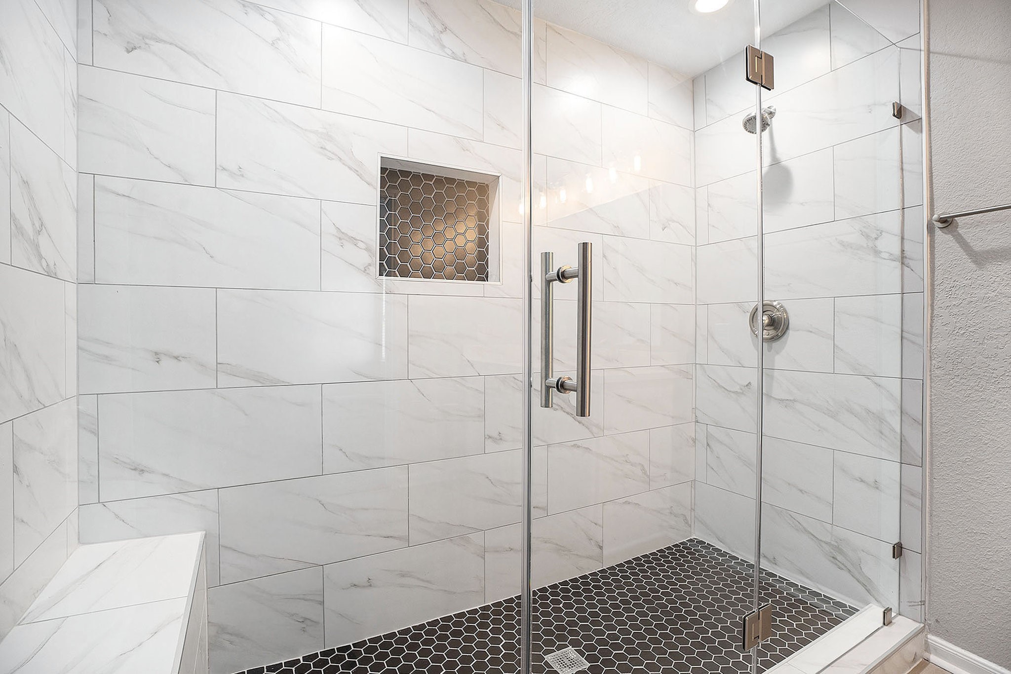 4027 Spurwing Lane Baytown, TX 77521 - Photo 25 of 34 This modern primary bathroom features a spacious glass-enclosed shower with elegant white tiles and a contrasting dark hexagonal tile floor. A built-in niche provides convenient storage space.