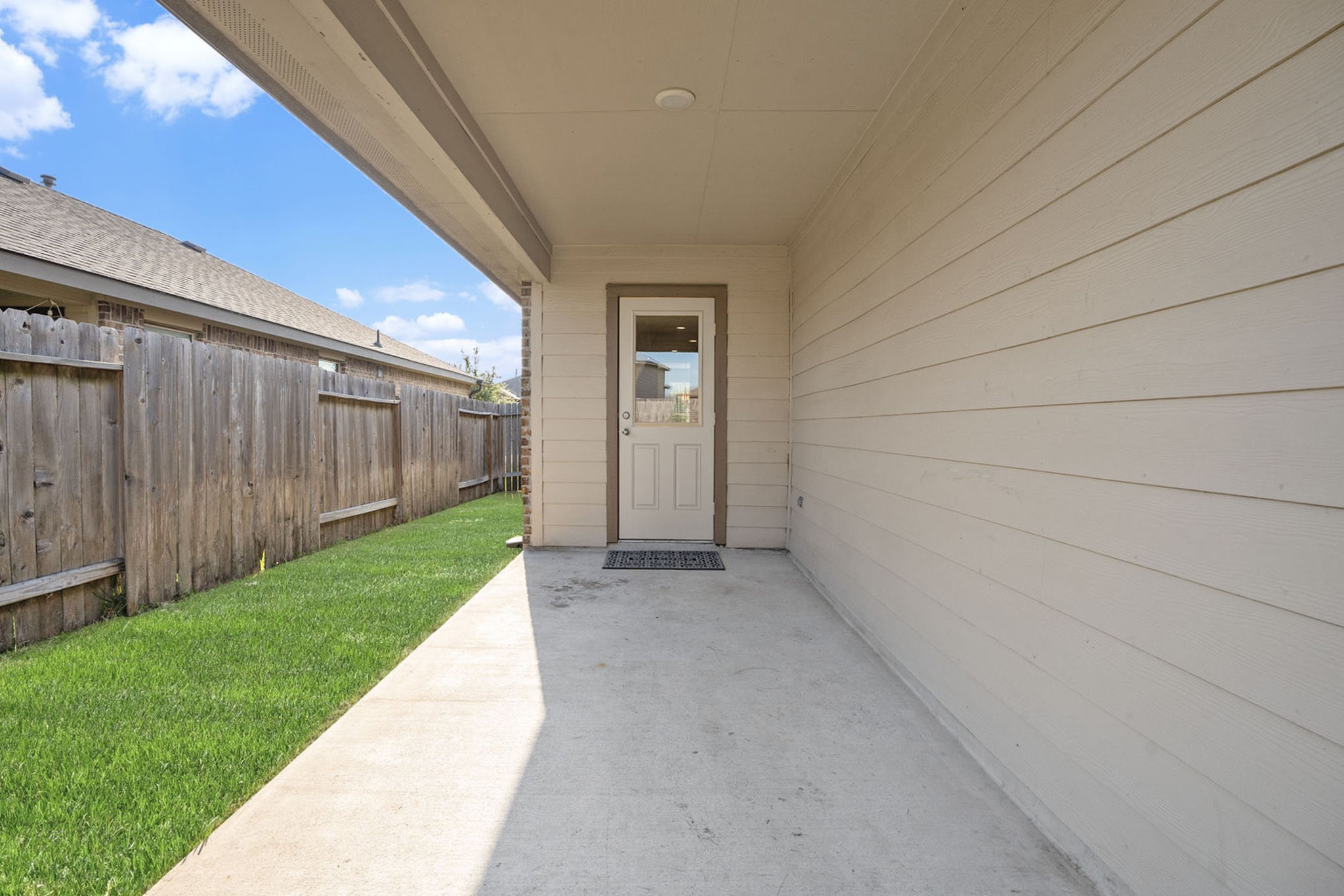 4027 Spurwing Lane Baytown, TX 77521 - Photo 28 of 34 This photo showcases a covered patio area with a concrete floor, leading to a back door. It features a fenced backyard with a well-maintained lawn, ideal for outdoor relaxation and privacy.