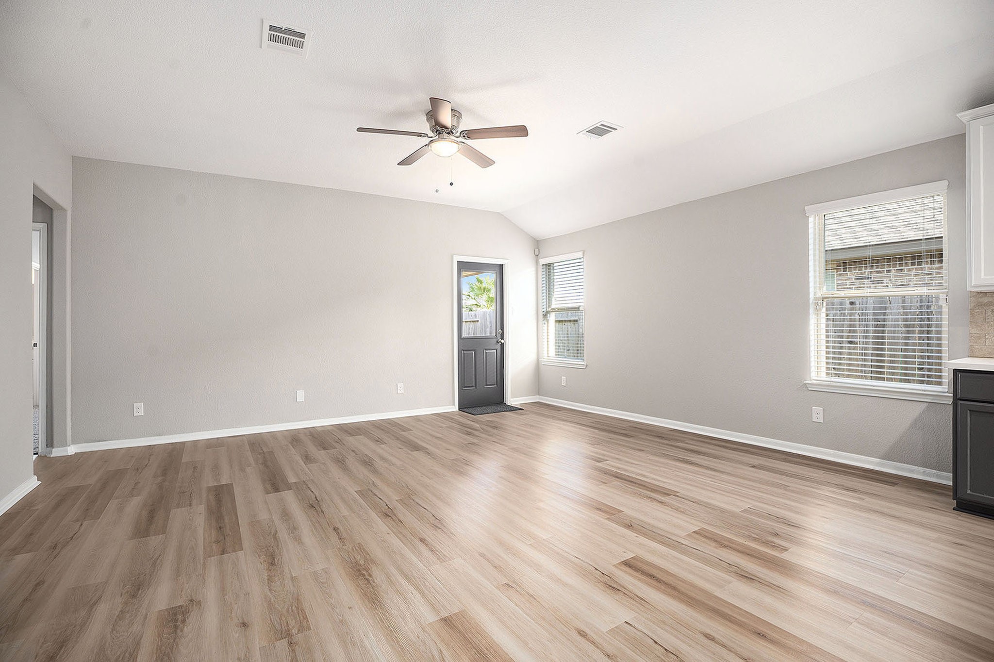4027 Spurwing Lane Baytown, TX 77521 - Photo 5 of 34 Spacious, bright living room with new flooring, freshly painted walls, a ceiling fan, and ample natural light from two windows and a door leading to a covered patio outside.