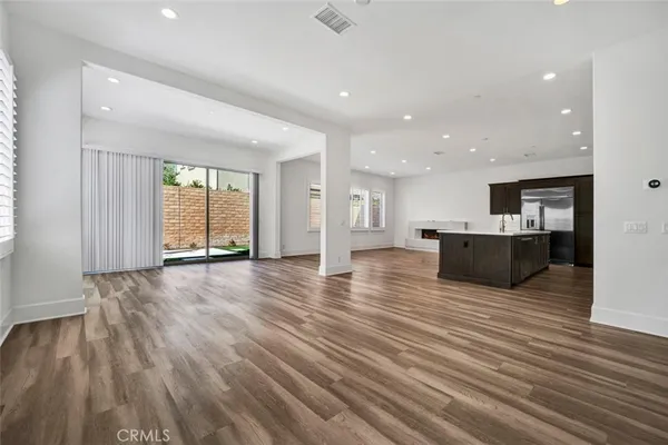 a view of an empty room with wooden floor and a kitchen
