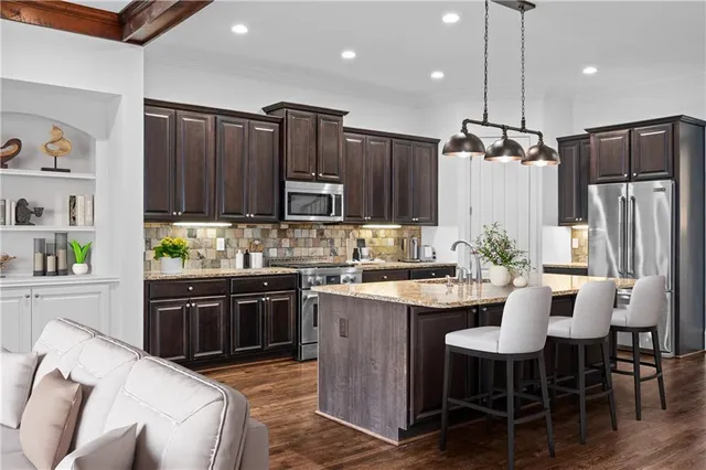 a kitchen with stainless steel appliances kitchen island granite countertop a refrigerator a stove a sink a dining table and chairs with wooden floor