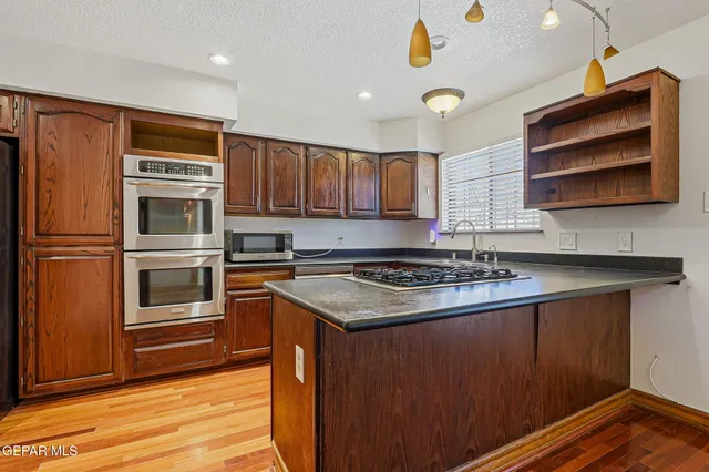 a kitchen with stainless steel appliances granite countertop a stove top oven a sink dishwasher and a microwave oven on the wooden floor