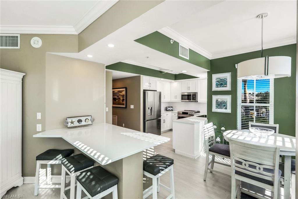 300 Dunes Boulevard, Unit 201 Naples, FL 34110 - Photo 13 of 50 a kitchen with stainless steel appliances kitchen island granite countertop a refrigerator a stove a dining table and chairs with wooden floor