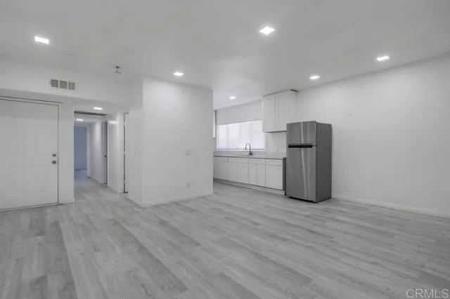 a view of an empty room with wooden floor and a kitchen