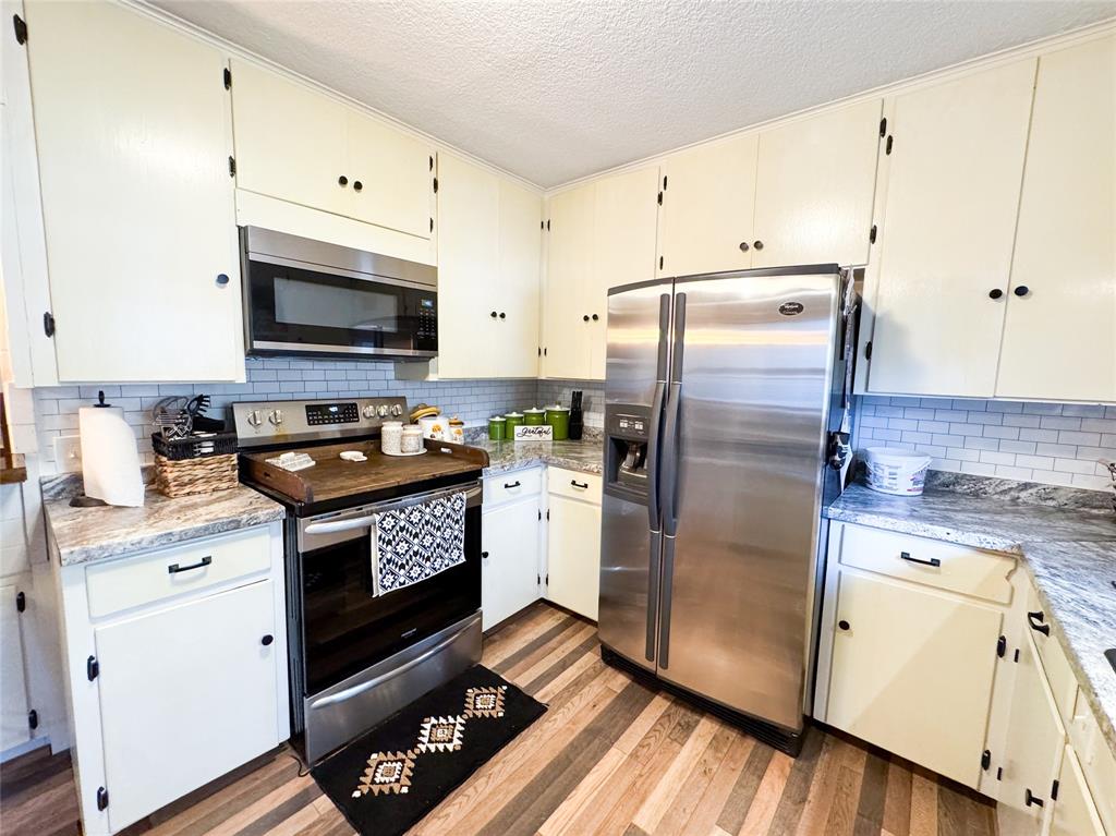 1303 Grand Central Avenue O'Brien, TX 79539 - Photo 12 of 40 a kitchen with granite countertop a refrigerator a sink and white cabinets