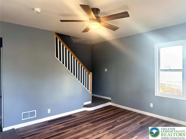 a view of an empty room with wooden floor and a ceiling fan