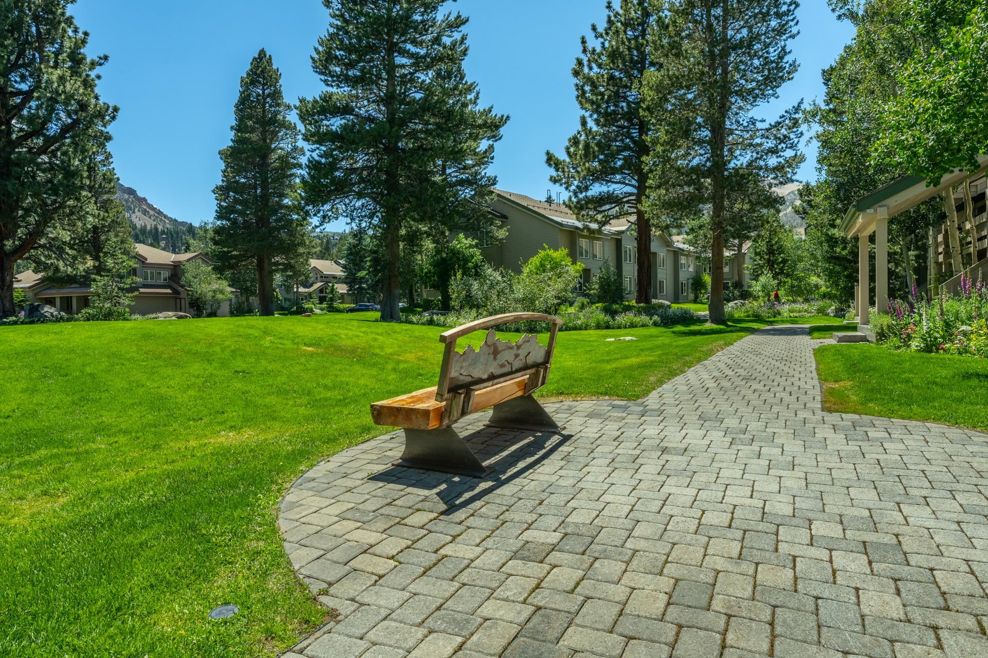 609 Golden Creek Road, Unit 609 Mammoth Lakes, CA 93546 - Photo 36 of 42 Expansive manicured lawn with mature evergreen trees, complemented by a paver pathway and a decorative wooden bench