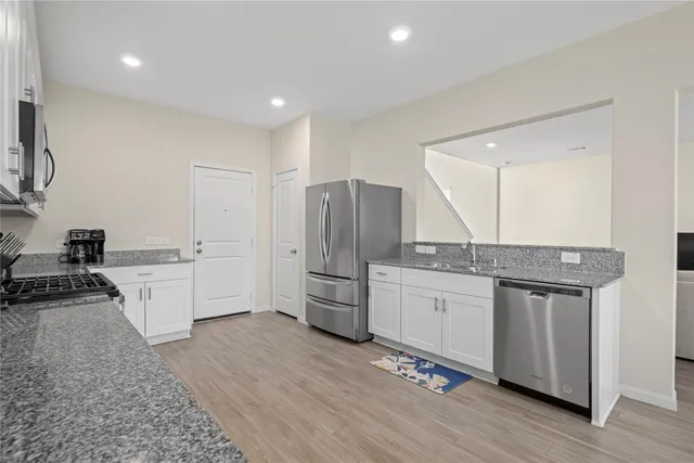 a large kitchen with a stove a sink dishwasher a refrigerator and white cabinets with wooden floor