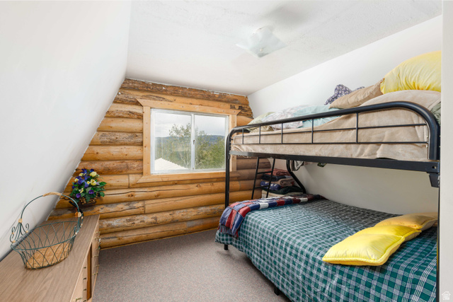 23 Scare Canyon, Unit 23 Logan, UT 84321 - Photo 14 of 33 Attic room with sloped white walls and log-style paneling, featuring a window with exterior visibility and light gray carpeting