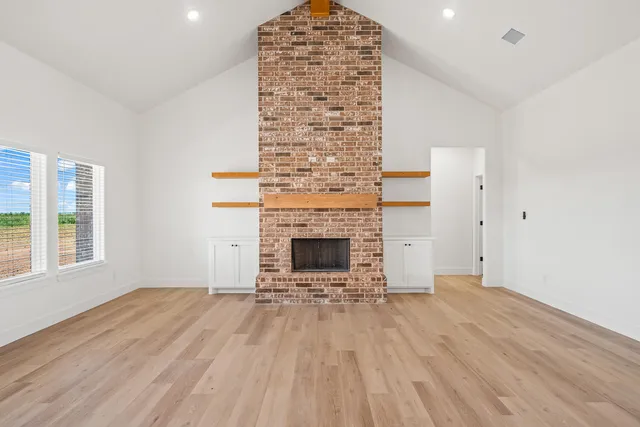 a view of an empty room with wooden floor fireplace and a window