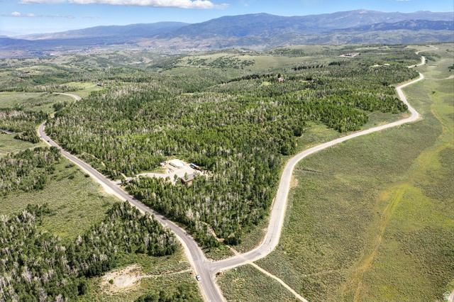 Expansive mountain property featuring significant tree coverage and clearings, a paved road network, and distant mountain ranges under a clear sky