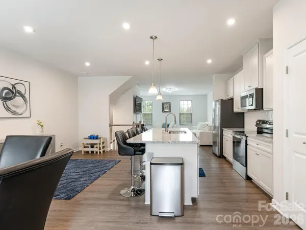 a dining room with stainless steel appliances kitchen island granite countertop a refrigerator a stove a sink and a dining table with wooden floor