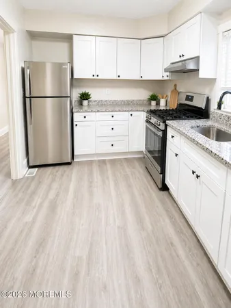 a kitchen with granite countertop a refrigerator sink and white cabinets