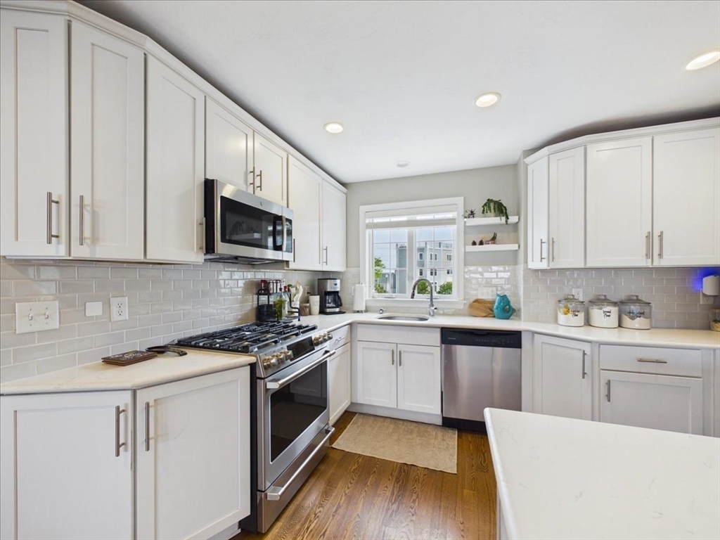 7 Bay Street, Unit 3 Hull, MA 02045 - Photo 15 of 40 a kitchen with stainless steel appliances granite countertop a stove top oven a sink dishwasher and white cabinets with wooden floor