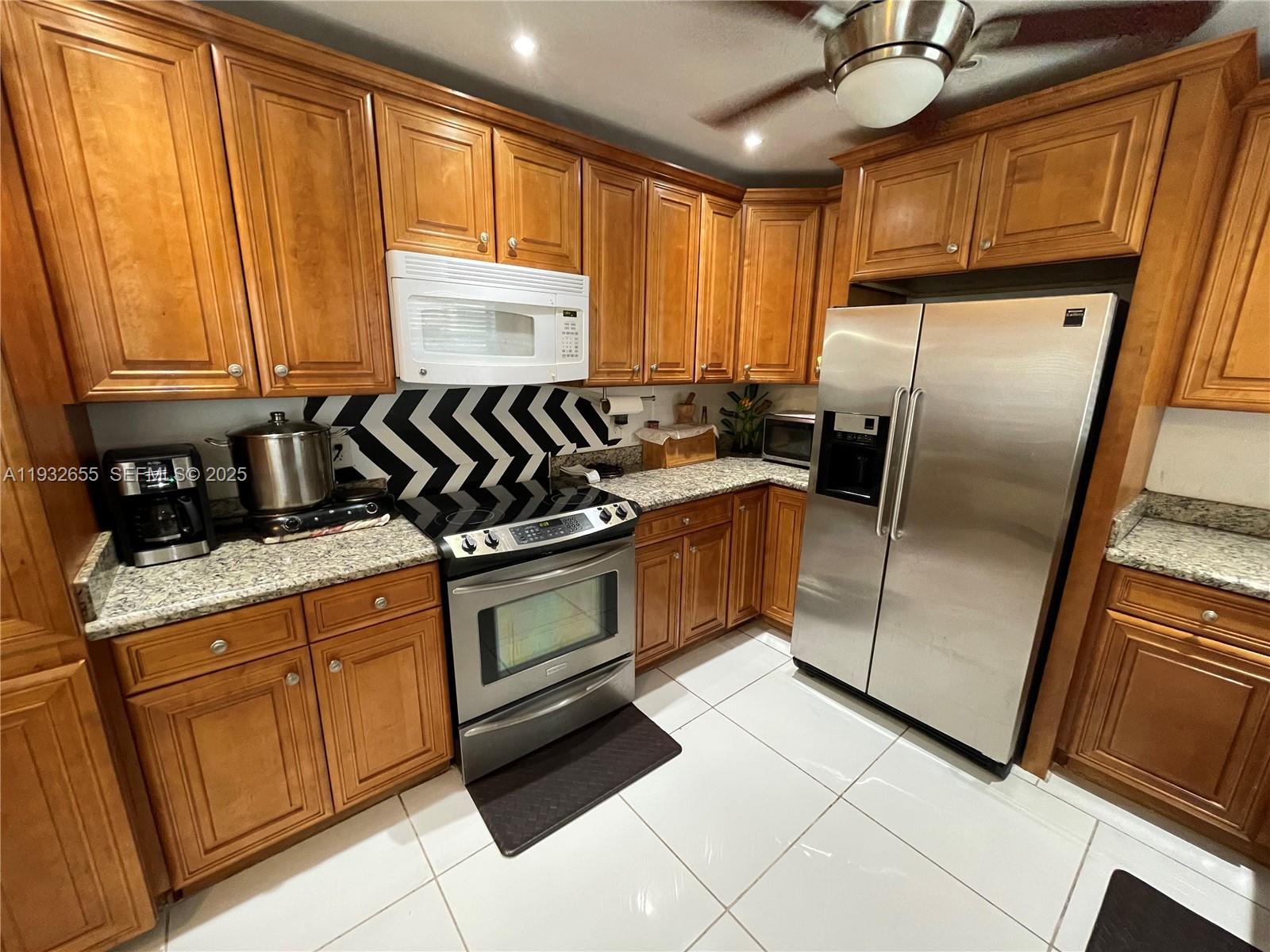 8951 Southwest 16th Street Boca Raton, FL 33433 - Photo 4 of 7 a kitchen with granite countertop a refrigerator a sink a stove and cabinets