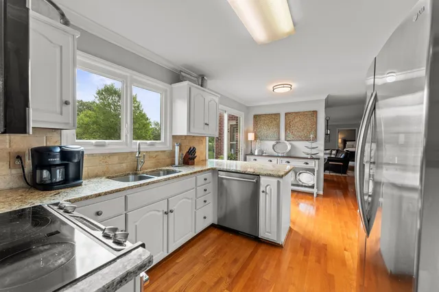 a kitchen with stainless steel appliances granite countertop a stove a sink dishwasher a refrigerator and white cabinets with wooden floor